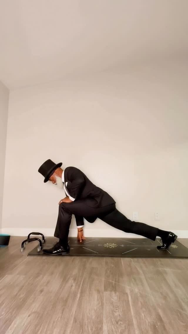 Rafael in a full suit and top hat holding a deep lunge on his yoga mat